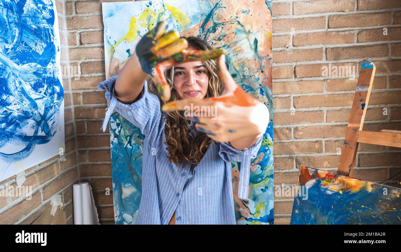 Nahaufnahme einer lächelnden Frau in ihrem Künstlerstudio, die Leinwand mit den Händen simuliert – ein junger Kunststudent, der in die Kamera schaut und lächelt Stockfoto