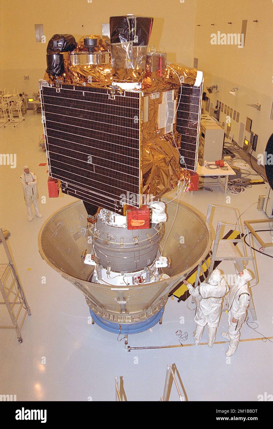 Mitarbeiter des Jet Propulsion Laboratory (JPL) in der Payload Hazardous Servicing Facility (PHSF) bereiten die Raumsonde Mars Global Surveyor auf die Startplatte vor, indem sie sie in einen Schutzbehälter stellen. Die Surveyor-Raumsonde (oben) ist bereits mit ihrem festen Treibgas-Oberstufen-Booster (unten) verbunden, der eigentlich die dritte Stufe des entbehrlichen Trägerfahrzeugs Delta II ist, das das Raumschiff auf seiner interplanetaren Reise zum Roten Planeten antreibt. Einmal auf dem Launch Pad 17A auf der Cape Canaveral Air Station werden die Raumfahrzeuge und die Booster-Baugruppe auf dem Delta-Fahrzeug gestapelt. Das S Stockfoto