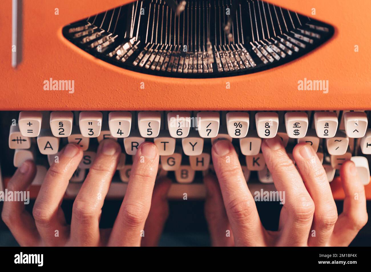 Nahaufnahme von Händen, die an einer orangefarbenen Vintage-Schreibmaschine arbeiten. Literarischer Schriftsteller Stockfoto