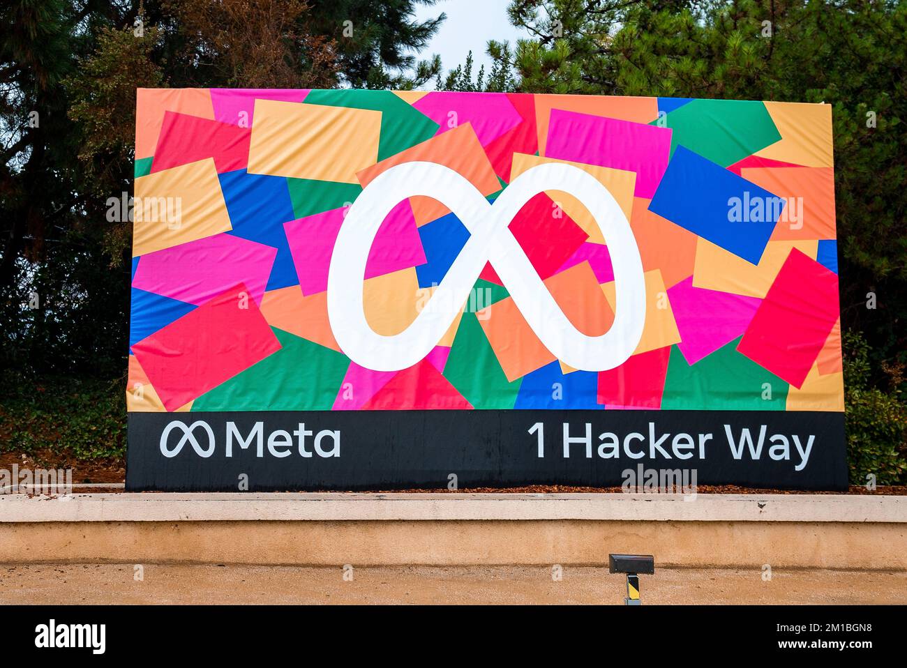Farbenfrohe Reklametafel mit Meta-Logo und 1-Hacker-Text vor Bäumen Stockfoto
