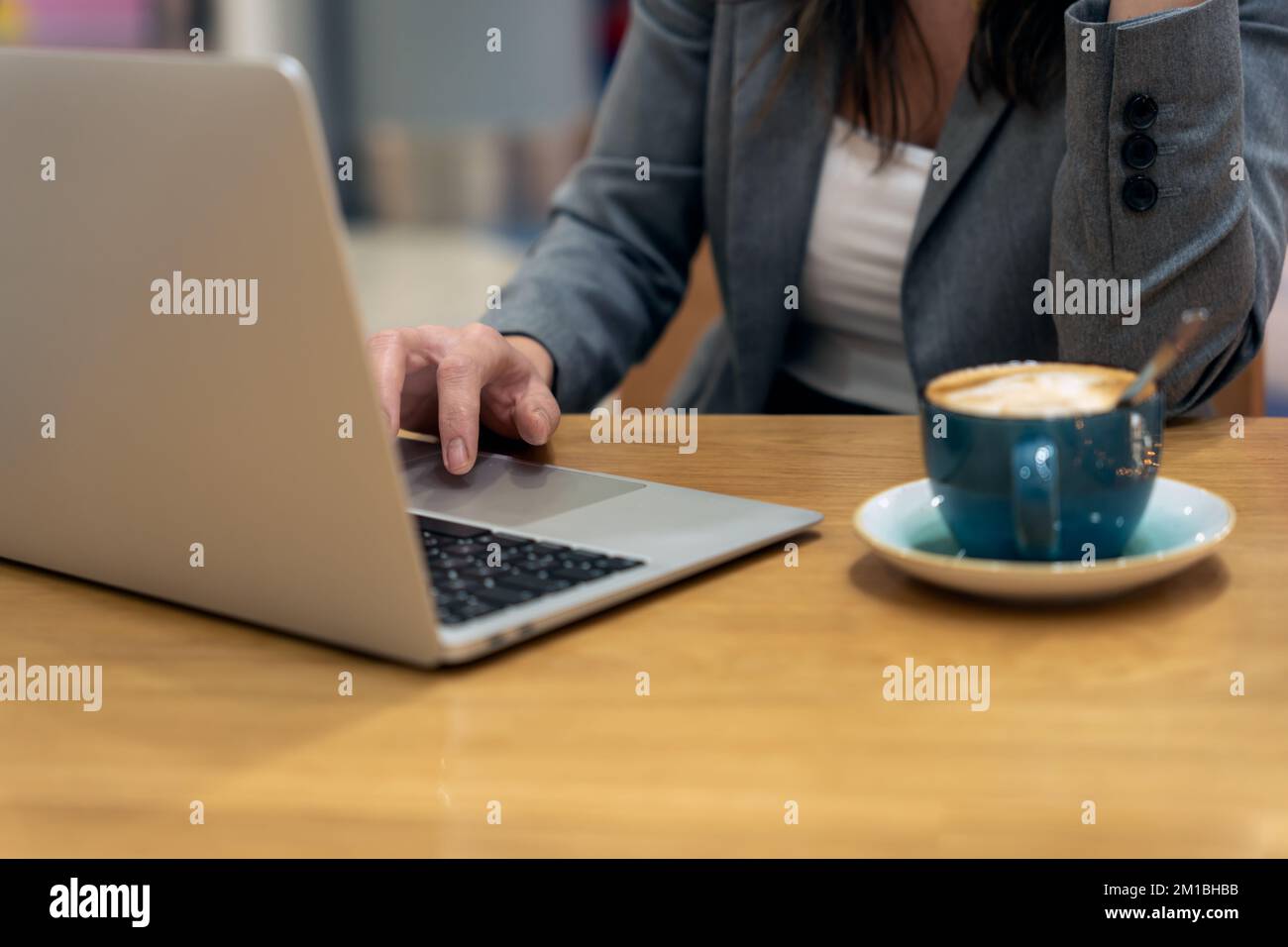 Anonyme weibliche Führungskraft, die mit dem Touchpad Daten auf einem Netbook in der Nähe einer Tasse Latte scrollt, während sie am Tisch sitzt und an einem Geschäftsprojekt arbeitet Stockfoto