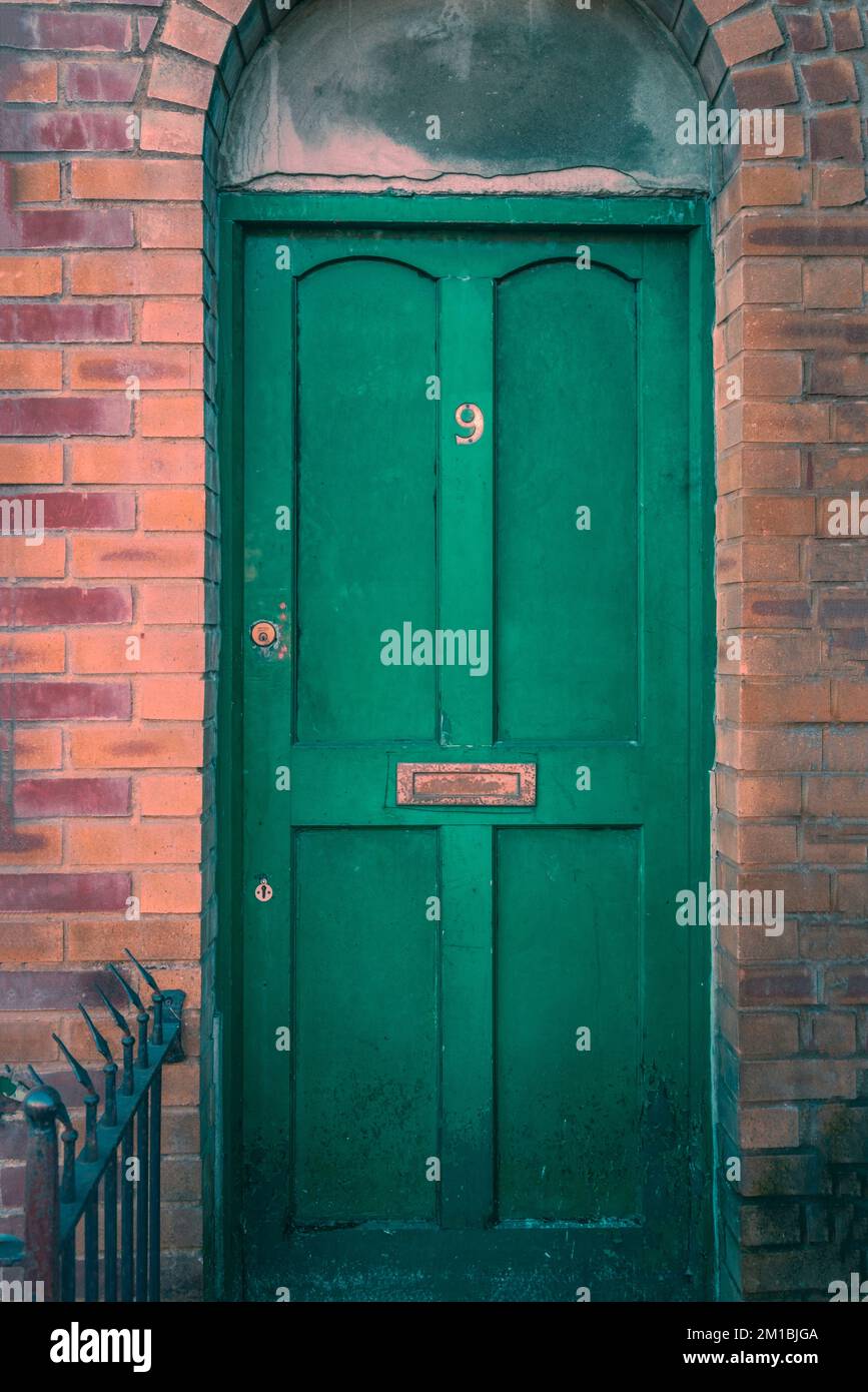 Grüne Eingangstür zu einem Haus mit Nummer neun-Nummernschild, umgeben von orangefarbenen und roten Ziegeln, England, Großbritannien Stockfoto