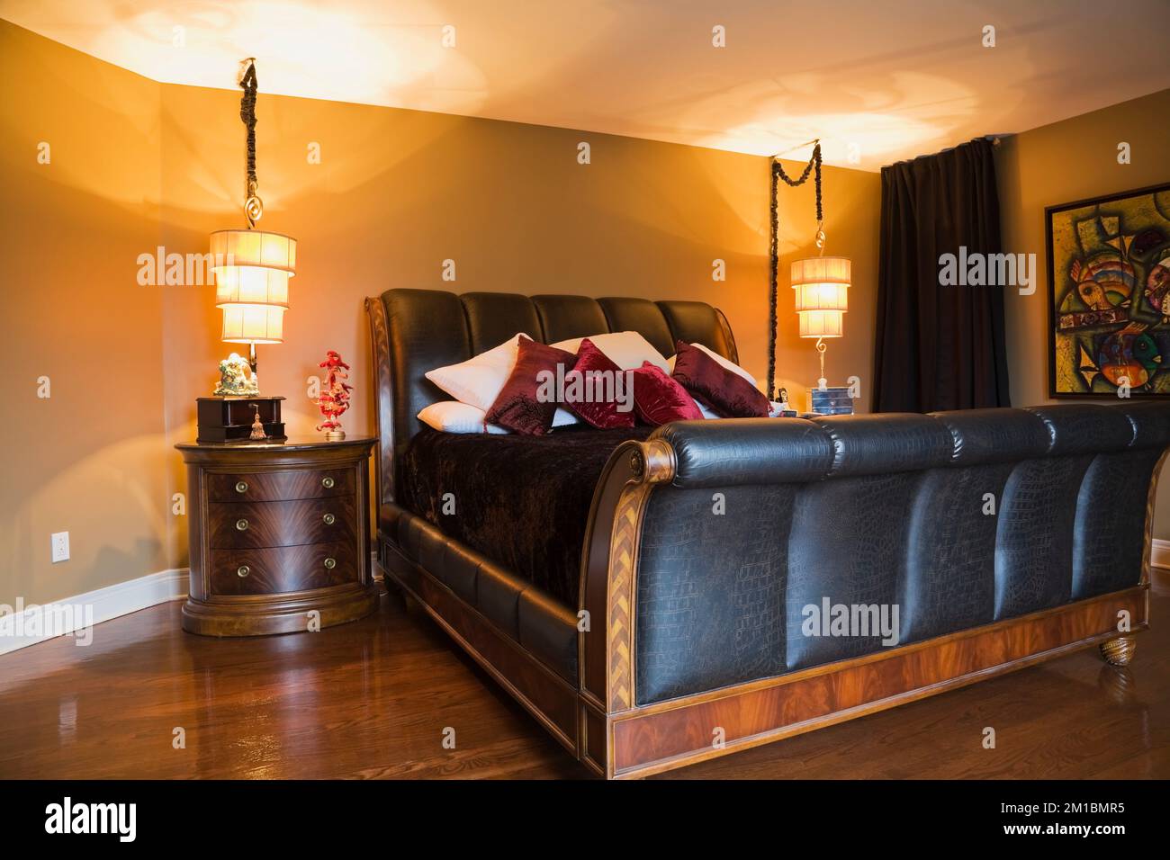 Kingsize-Bett aus Holz und Leder, Schlittenbett und Nachttisch im Hauptschlafzimmer mit braunen gelb bemalten Wänden im oberen Stockwerk im luxuriösen Haus. Stockfoto