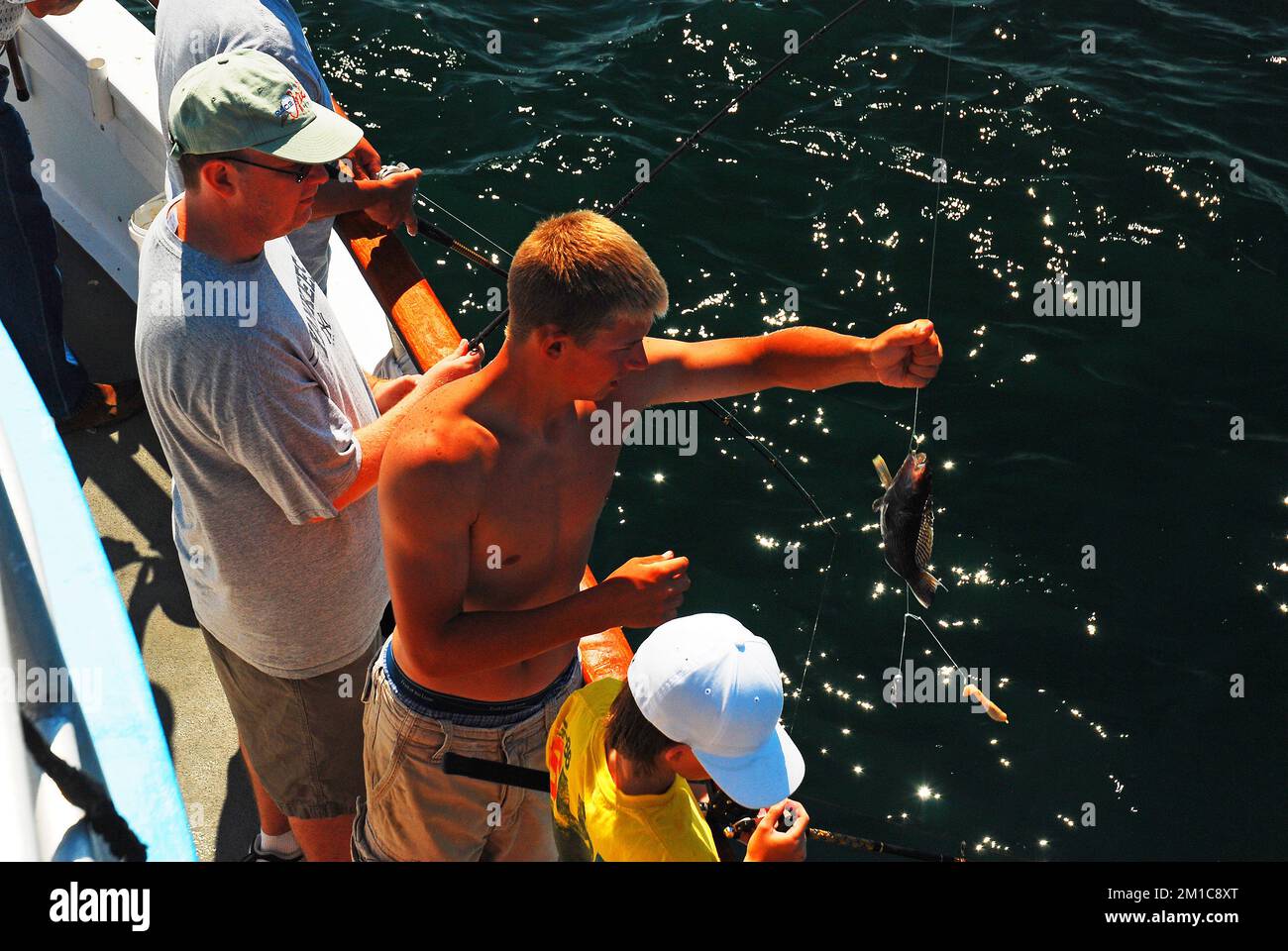 Ein junger Mann hilft einem Fischer, seinen Fang auf einem gecharterten Fischerboot vor der Küste von Long Island einzuholen Stockfoto