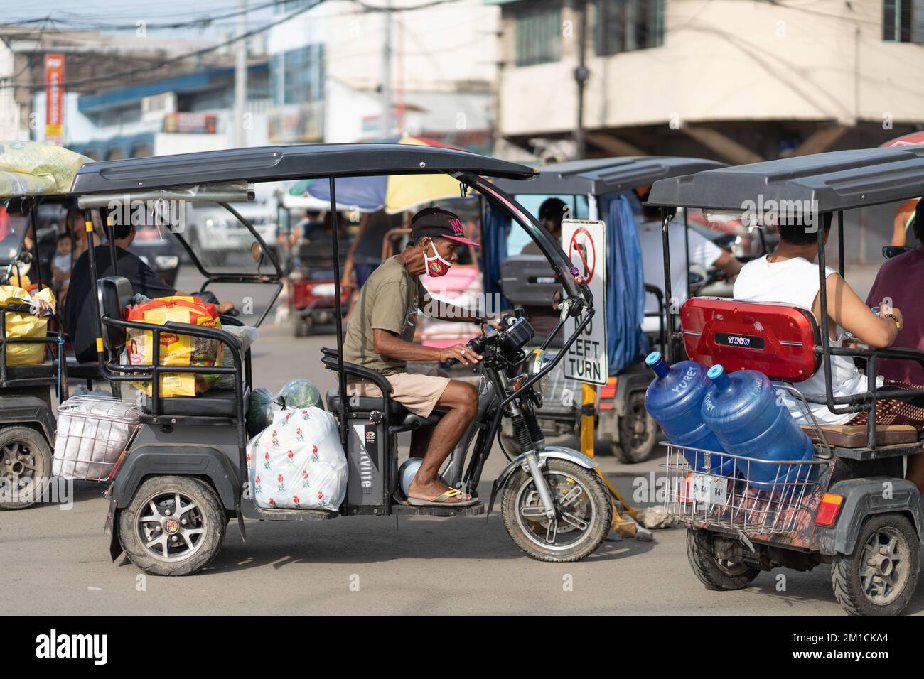 Ein Mann, der ein Elektrofahrzeug mit drei Kilo fährt. Diese sind in den Außenbezirken der Stadt sehr verbreitet, wo sie die kleineren, überfüllten Straßen durchqueren können. Stockfoto
