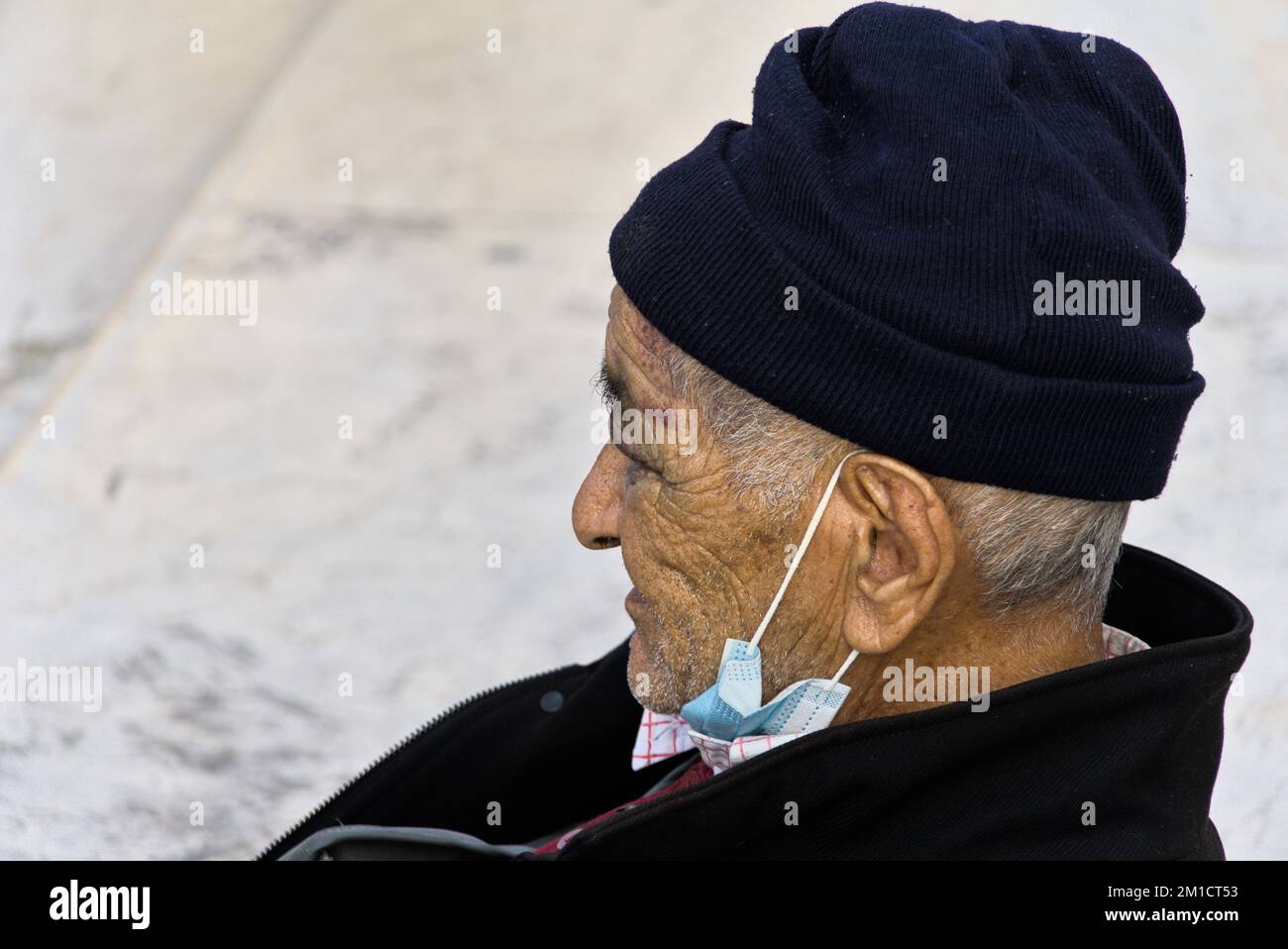 Ein alter Mann mit schwarzem Hut und einer Maske unter dem Kinn. Stockfoto