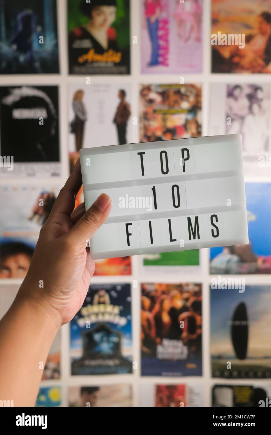 Die weibliche Hand hält die Miniatur-Kino-LED-Lichtbox mit Filmpostern an der Wand. Buchstaben schreiben Top-10-Filme. Vertikaler Hintergrund. Year-End-Listenkonzept. Stockfoto