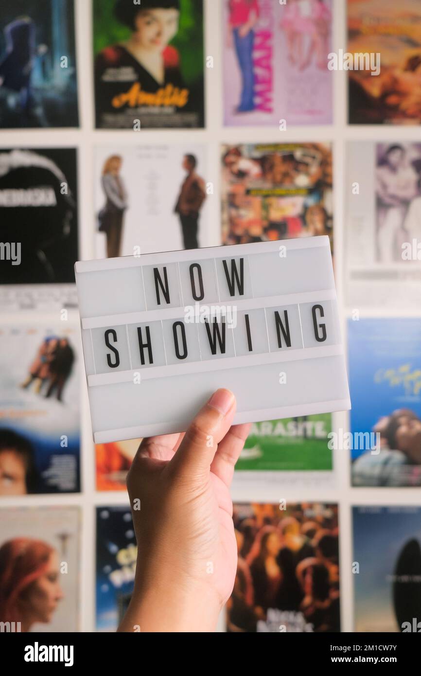 Die weibliche Hand hält die Miniatur-Kino-LED-Lichtbox mit Filmpostern an der Wand. Buchstaben werden jetzt angezeigt. Vertikaler Hintergrund. Das aktuelle Filmkonzept. Stockfoto