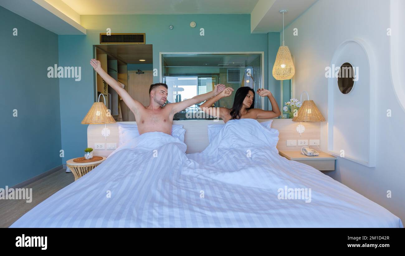 Ein paar asiatische Frauen und weiße Männer wachen in einem Hotelbett im Schlafzimmer auf. Stockfoto