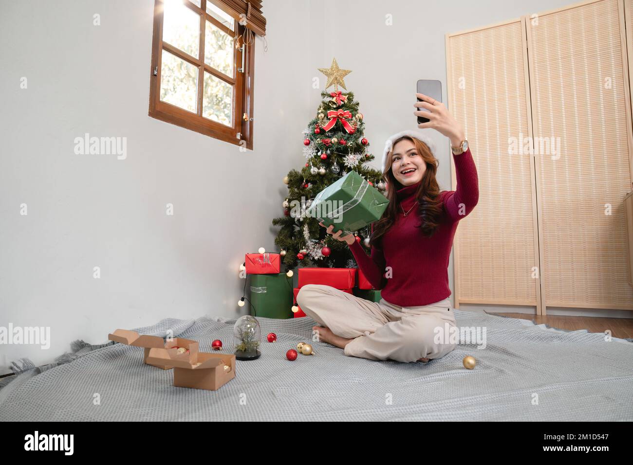 Weihnachtsselfie am Weihnachtsbaum. Glückliches junges Mädchen, das Selfie auf dem Smartphone in einem dekorierten Weihnachtsbaum-iat-Heim macht Stockfoto