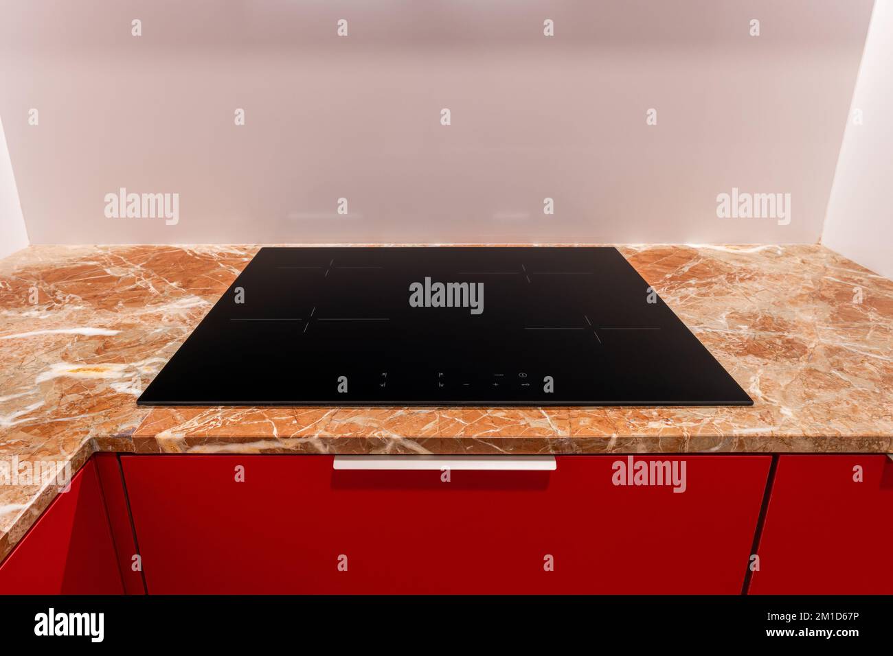 Das schwarze Induktionskochfeld mit vier Kochplatten ist in die beige Marmorablagefläche eines roten Küchenschranks eingebaut. Hellbraune Arbeitsplatte mit abstraktem Muster Stockfoto