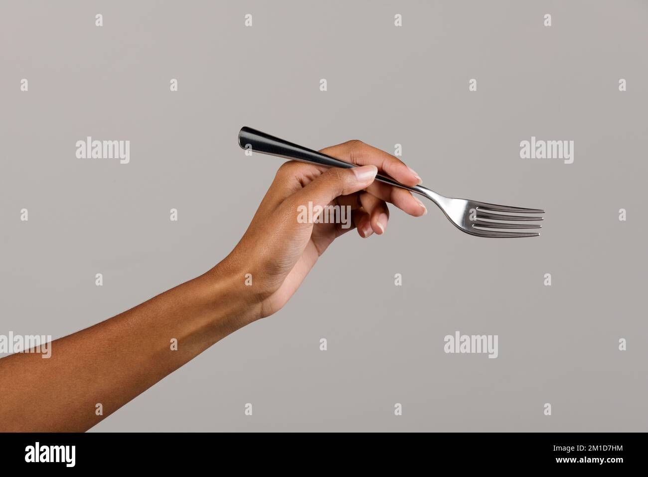 Eine anonyme afroamerikanische Frau mit einer silbernen Essensgabel aus Metall auf grauem Hintergrund ernten Stockfoto