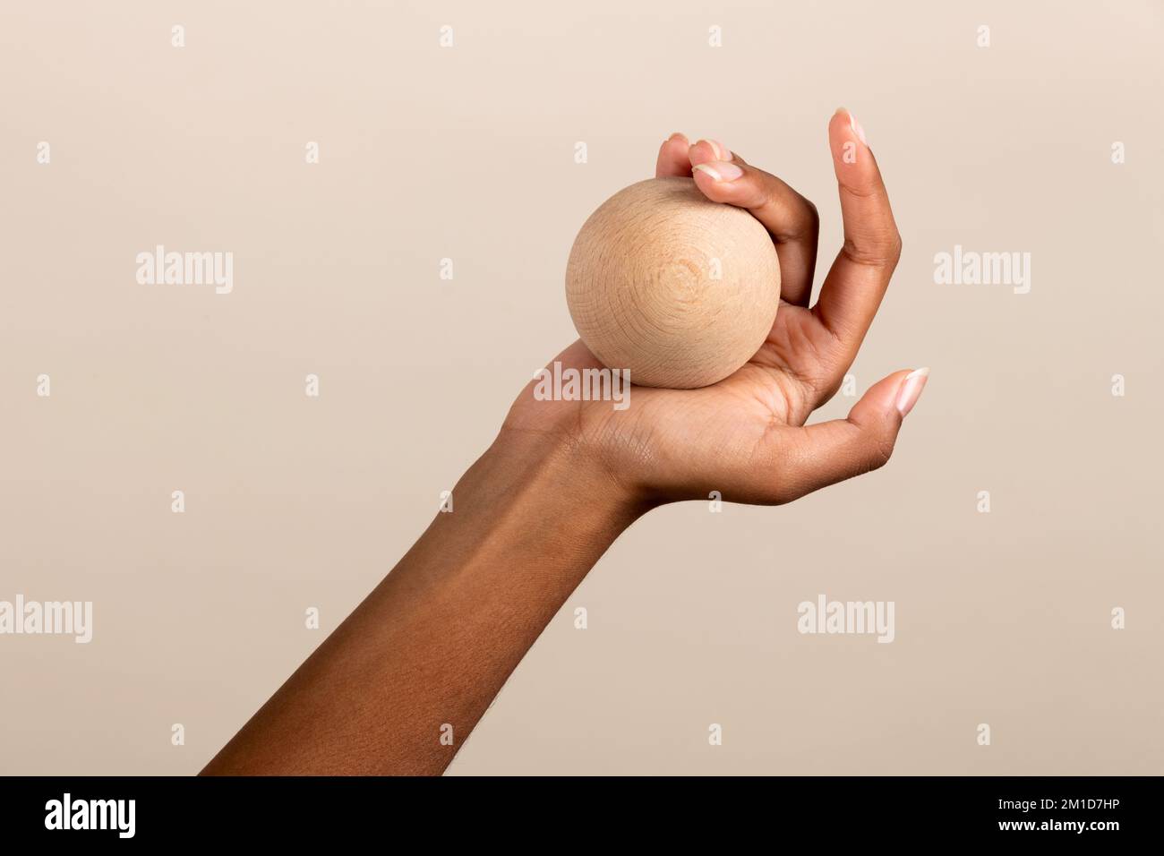 Eine anonyme afroamerikanische Frau zeigt eine kleine runde Holzkugel auf beigefarbenem Hintergrund Stockfoto