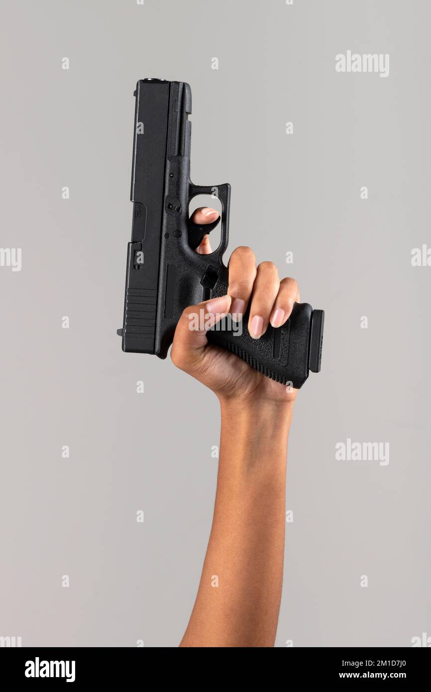 Anonyme afroamerikanische Frau mit schwarzer Handfeuerwaffe auf grauem Hintergrund im Studio Stockfoto