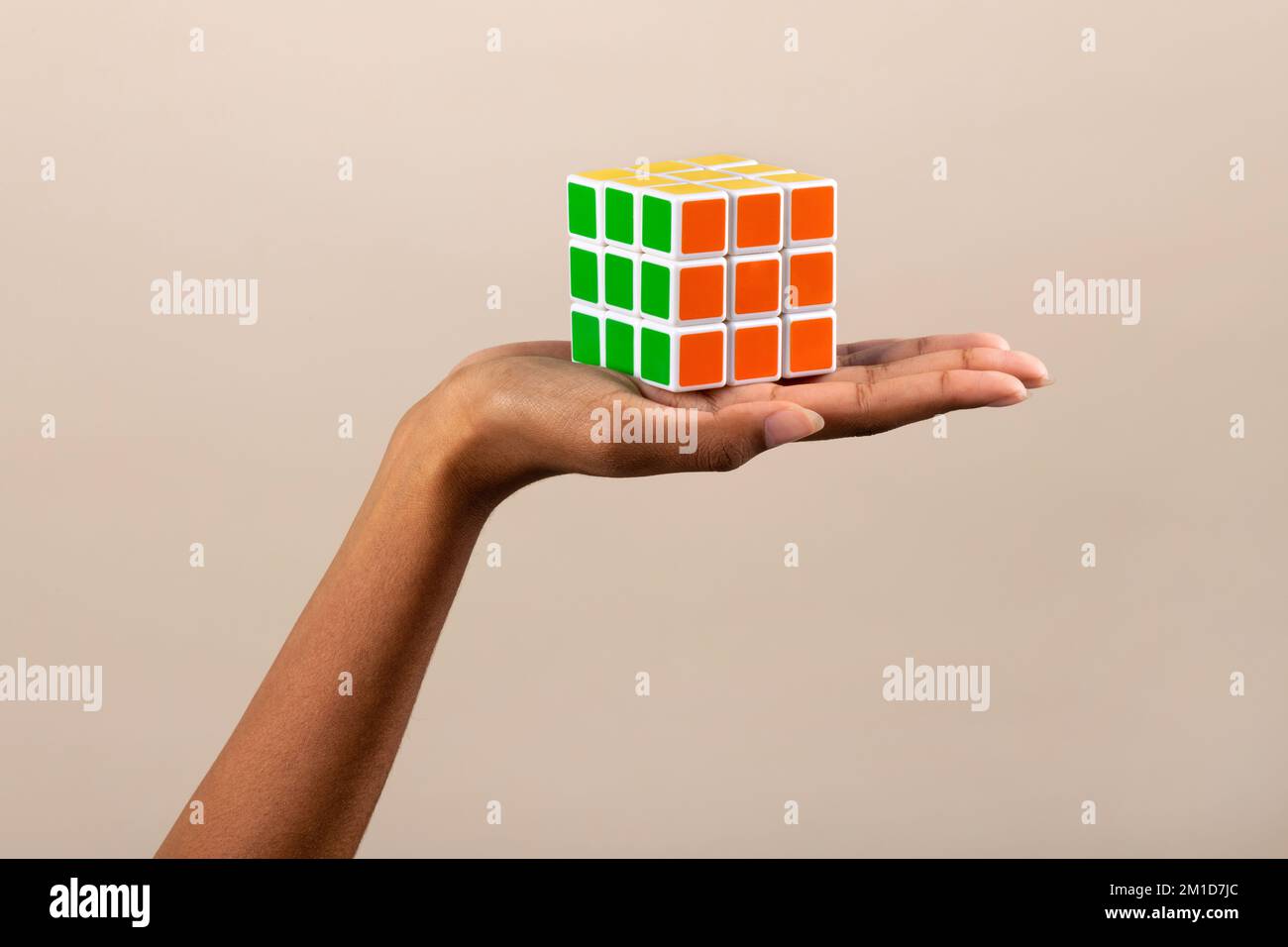 Unerkennbare afroamerikanische Frau, die aufgelösten, bunten Rubiks-Würfel auf beigem Hintergrund vorführt Stockfoto