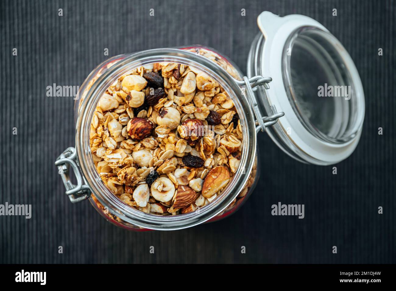 Konzept von hausgemachtem, handgemachtem geröstetem Müsli mit verschiedenen Nüssen und Rosinen in einem wunderschönen Glasgefäß, über der Aussicht. Schwarzer Textilhintergrund mit Platz. Stockfoto