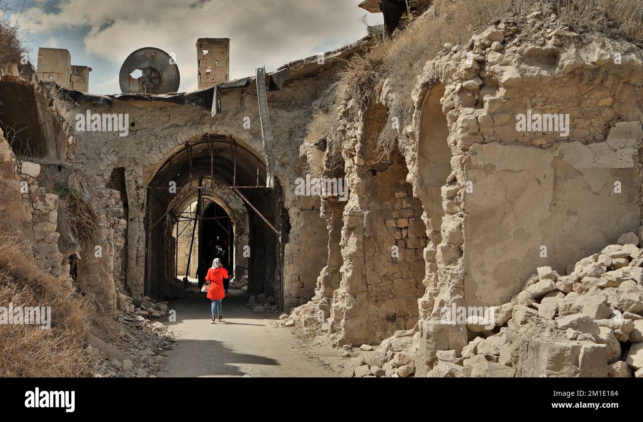 Eine Frau in einem roten Umhang und Hijab, die durch den zerstörten Souk, Aleppo, Syrien läuft Stockfoto