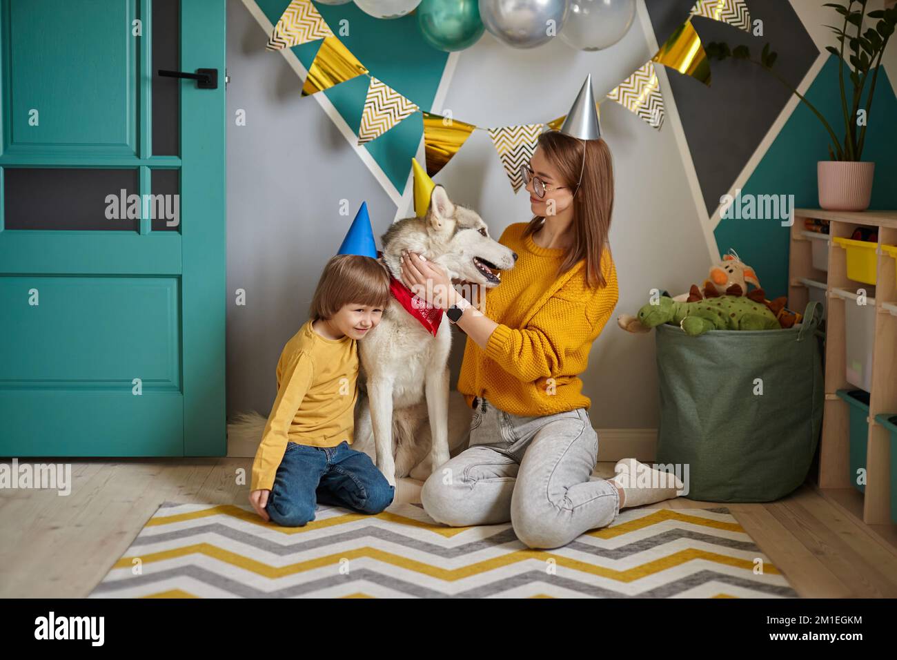 Hund Tiergeburtstag, Familienmutter und Kind umarmen ihren Hund und gratulieren ihm zum Geburtstag Stockfoto