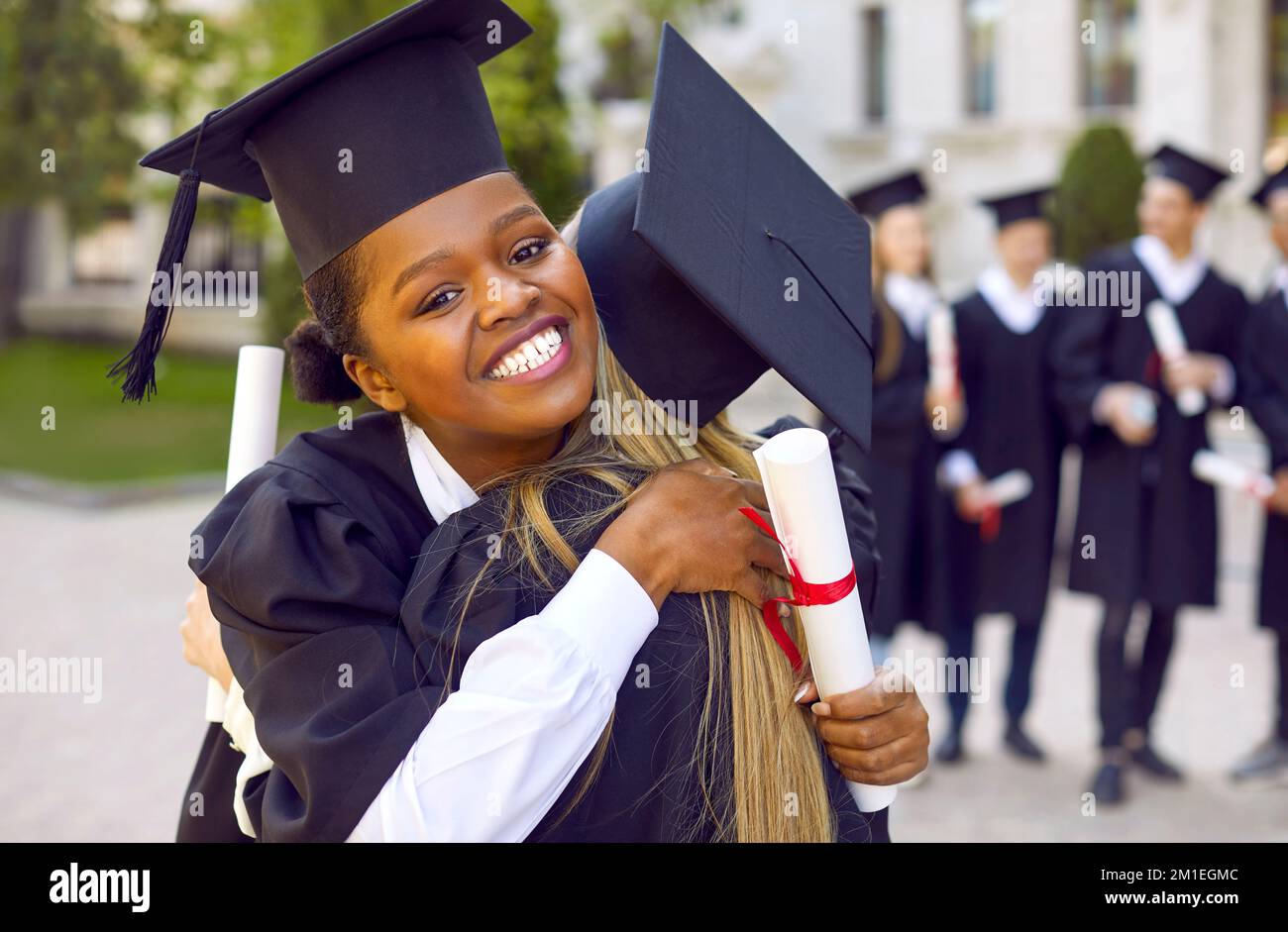 Zwei glückliche Studentinnen, die sich während der Abschlussfeier an der Uni umarmen. Stockfoto