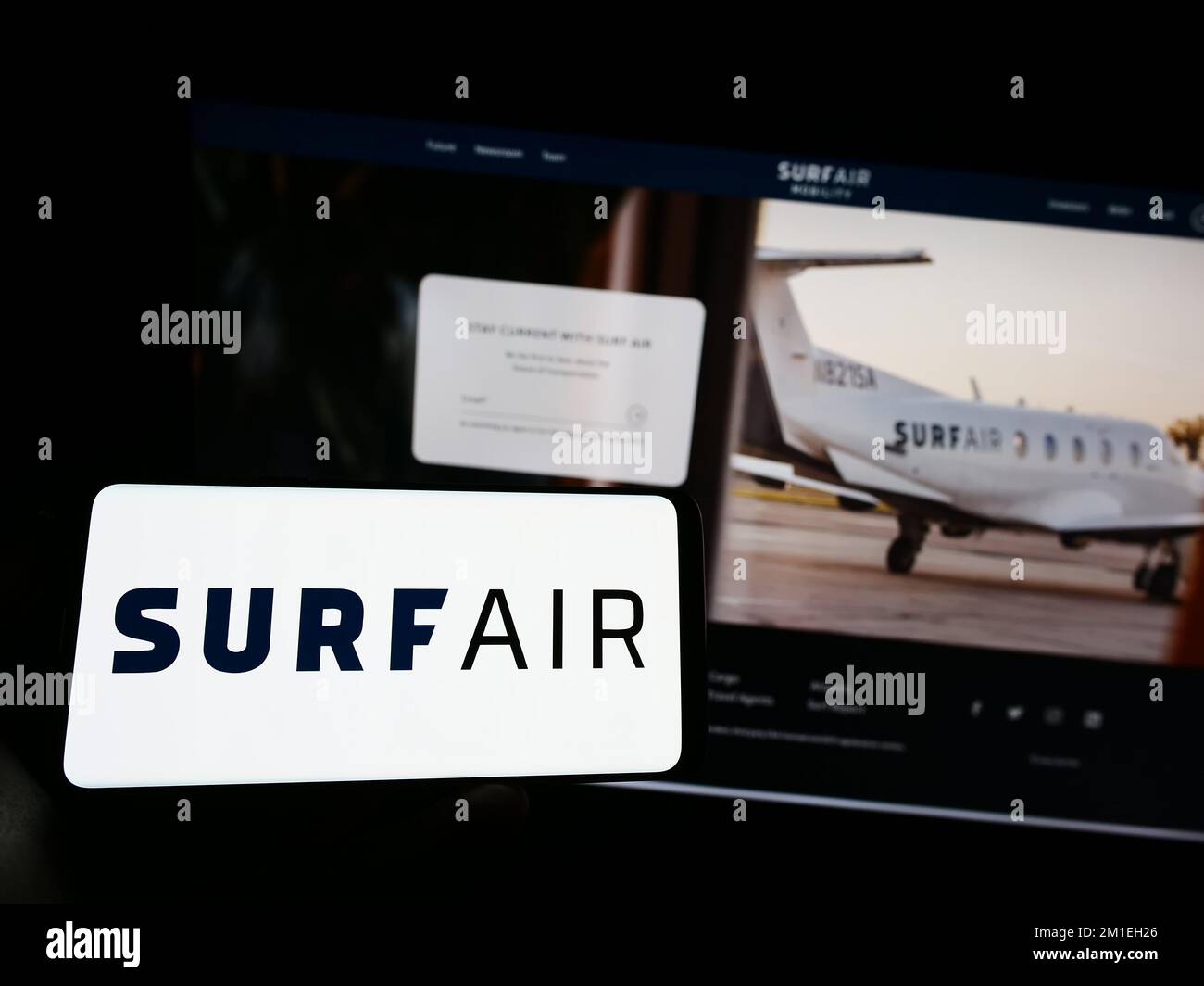Person, die ein Mobiltelefon mit dem Logo des amerikanischen Luftfahrtunternehmens Surf Air Mobility auf dem Bildschirm vor der Webseite hält. Konzentrieren Sie sich auf das Display des Telefons. Stockfoto