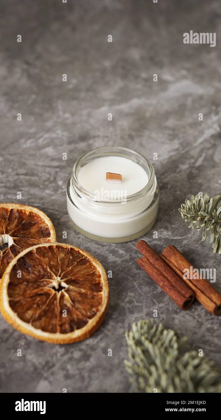 Aromatherapie. Kerze in einem Glas mit Scheiben von Orange, Zimtstangen und Tannenzweigen. Moderne hausgemachte Kerze mit Docht aus Holz. Vertikales Foto Stockfoto