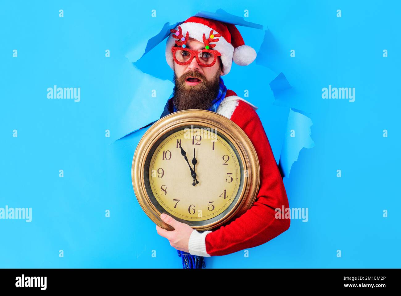 Überraschter Weihnachtsmann mit alter Uhr, die durch das Papierloch blickte. Bereiten Sie sich auf Weihnachten oder Neujahr vor. Stockfoto