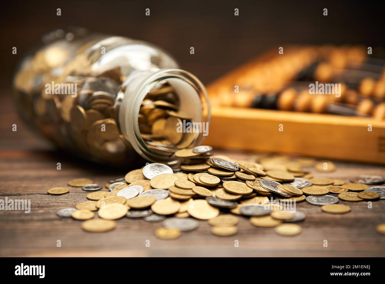 Glasbehälter mit goldenen Münzen und Abakus auf Holzhintergrund. Geld, Finanzen, Investitionskonzept Stockfoto