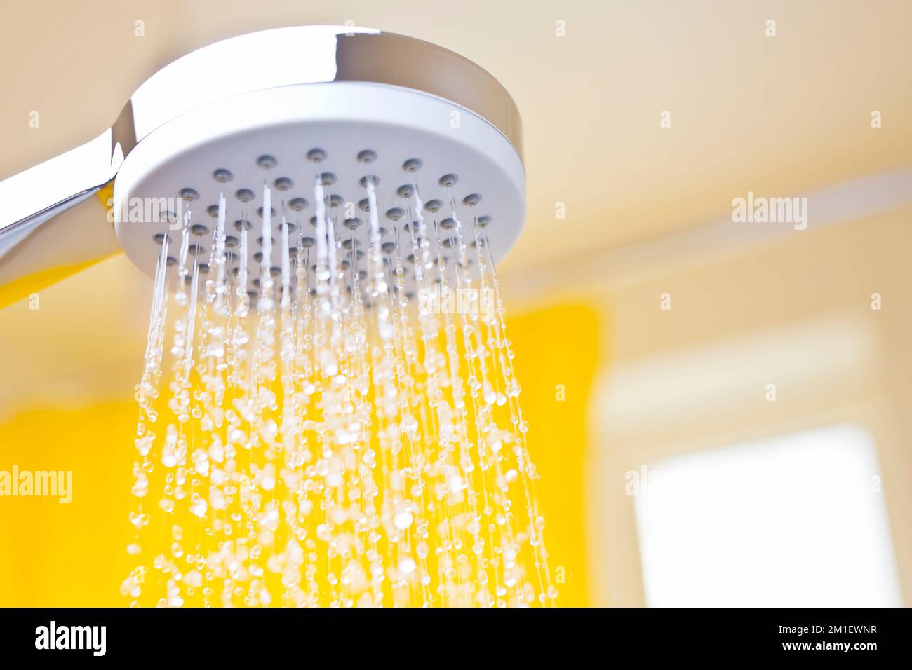 Nahaufnahme fließender Wassertropfen aus einem Duschkopf in einem hellen Badezimmer mit gelbem Hintergrund Stockfoto