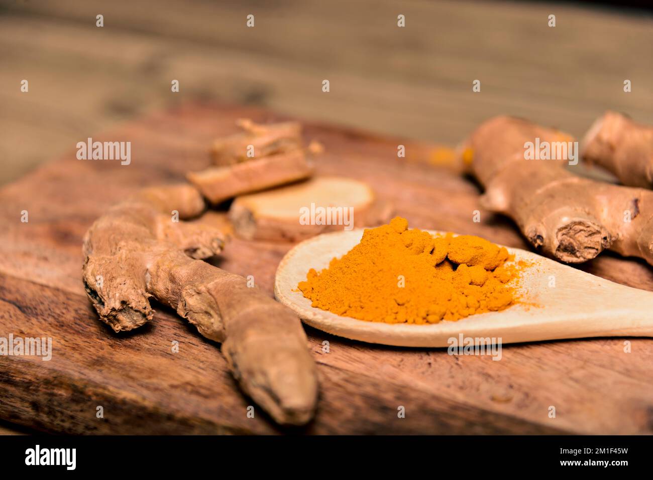 Nahaufnahme Kurkuminpulver in Holzlöffel mit frischem Rhizom auf Holzhintergrund Stockfoto