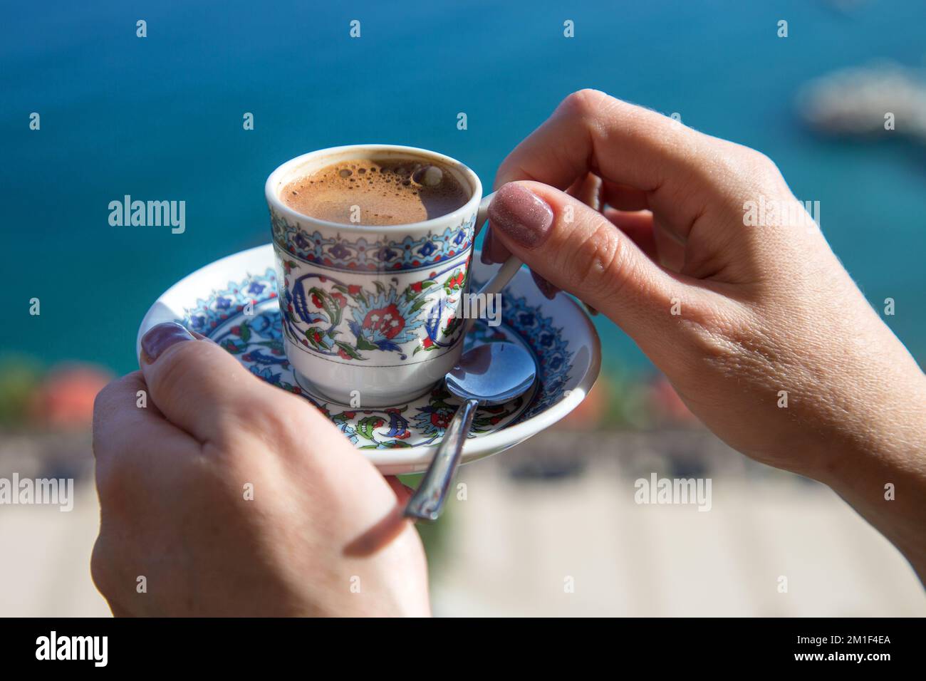 Die Hand einer Frau, die eine Tasse mit einer Untertasse türkischen Kaffees hält, vor dem Hintergrund des blauen Meeres. Stockfoto