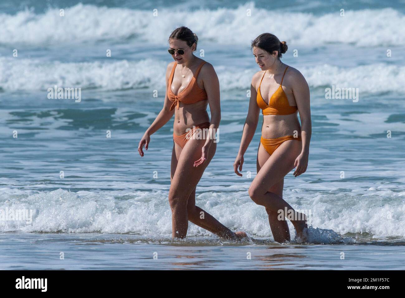 Zwei Weibchen in Bikinis, die am Fistral Beach in Newquay in Cornwall in Großbritannien aus dem Meer laufen. Stockfoto