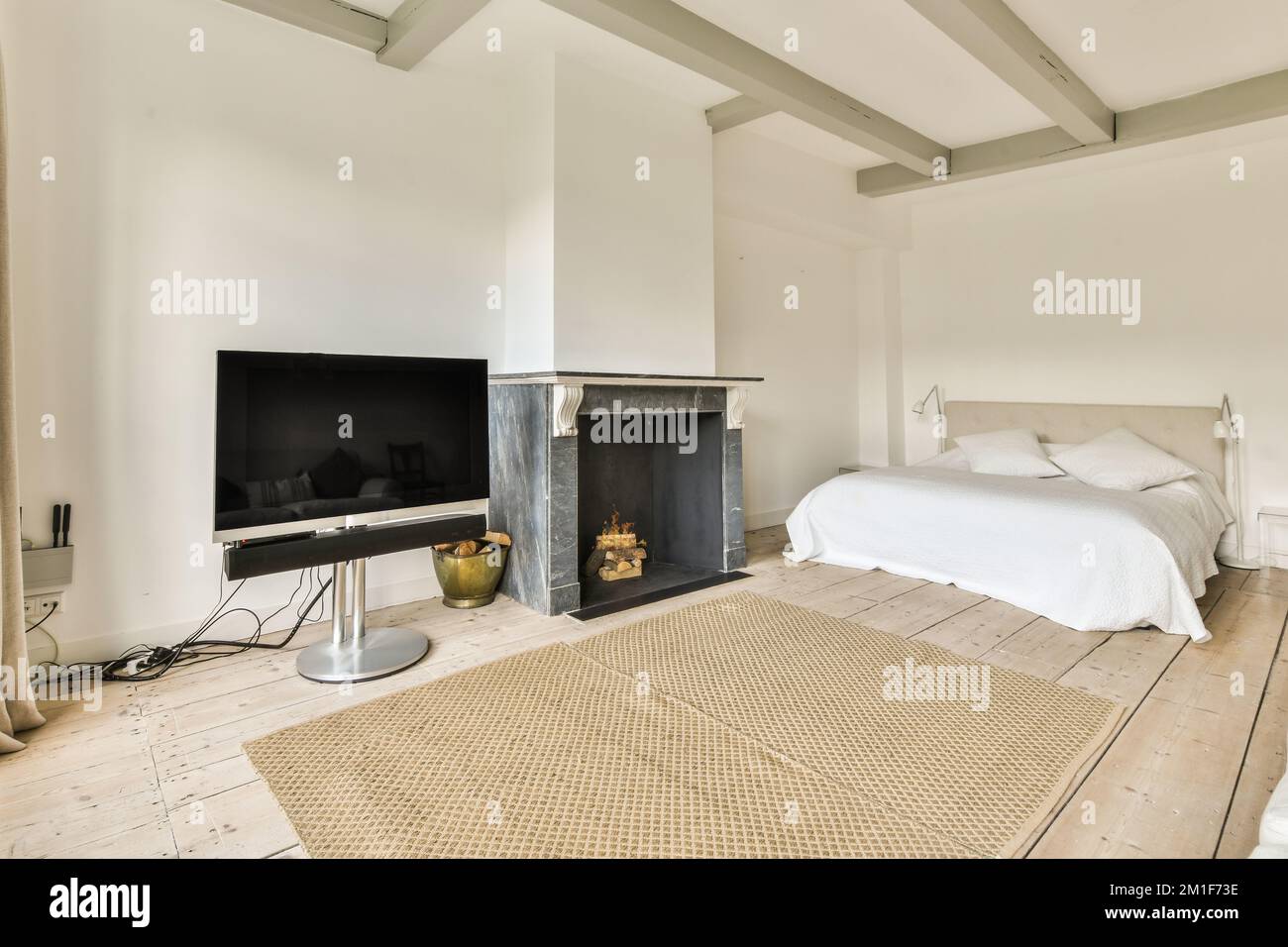 Modernes Bett mit komfortabler Matratze und Sofa in der Nähe von Fernseher und Kamin im geräumigen Schlafzimmer Stockfoto