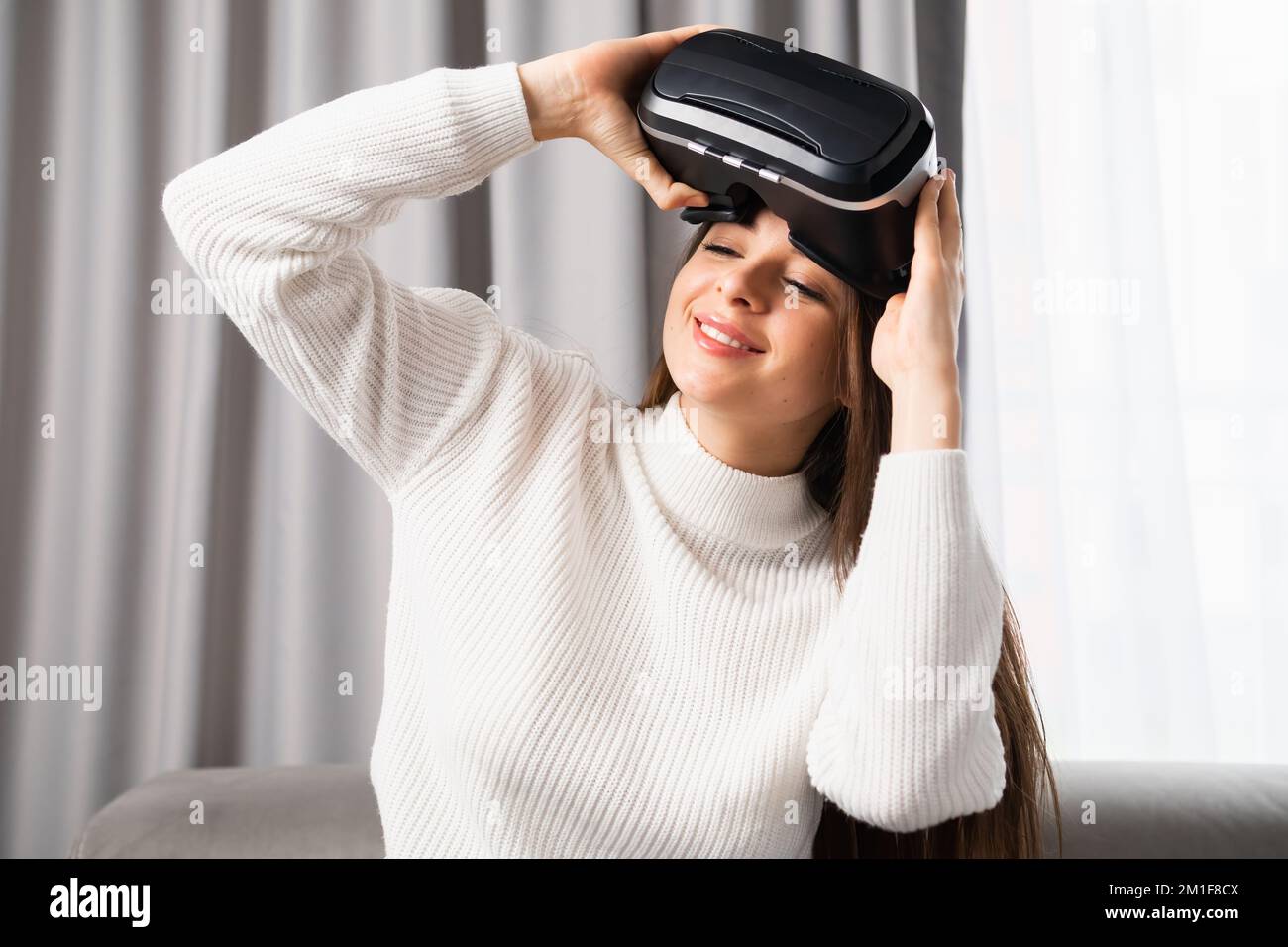 Porträt einer lächelnden Frau, die eine VR-Brille aufsetzt, um Spiele im Cyber-Raum zu spielen. Stockfoto