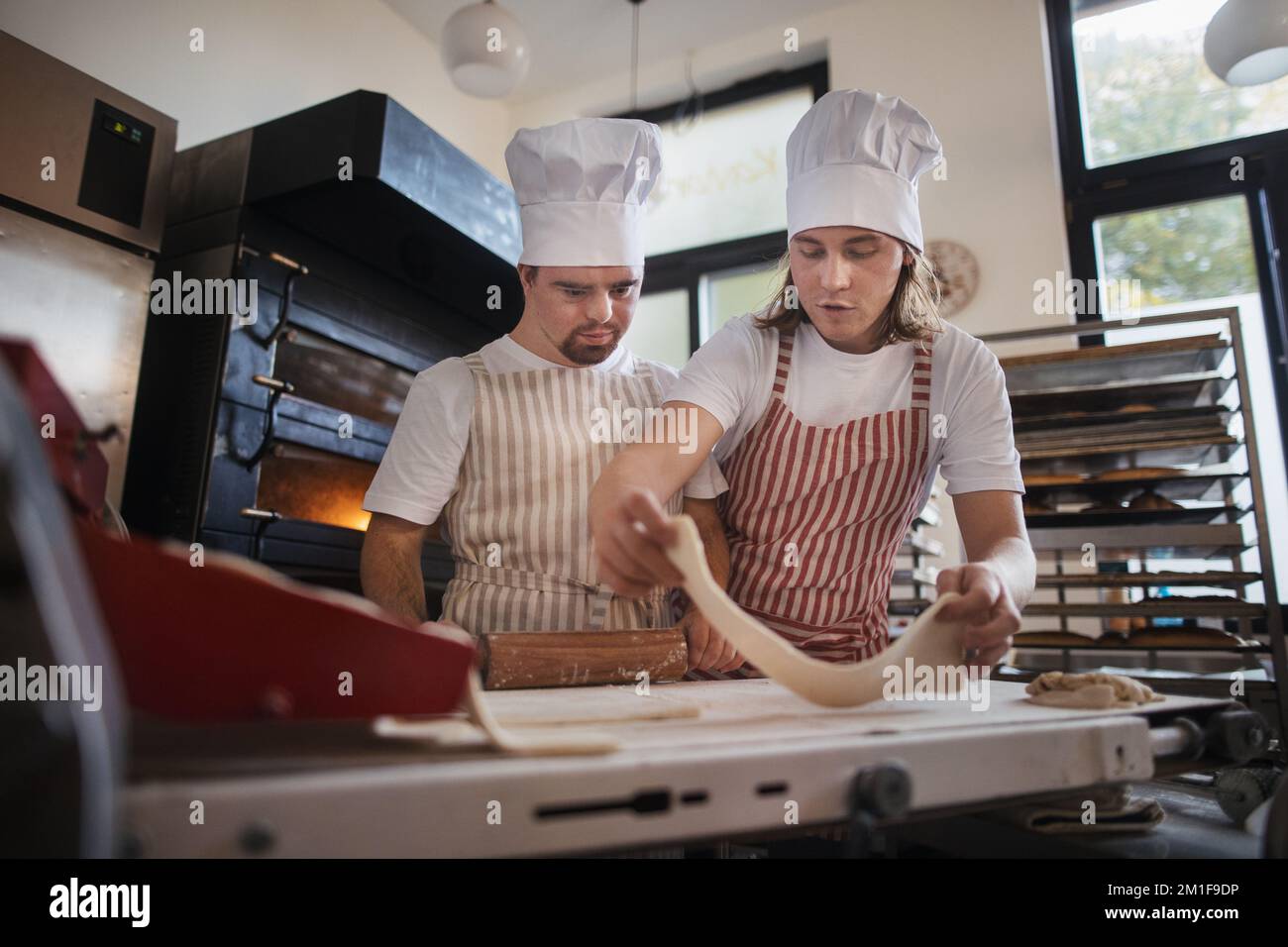 Ein Mann mit daunensyndrom, der mit seinem Kollegen Brot in der Bäckerei vorbereitete. Konzept der Integration von Menschen mit Behinderungen in die Gesellschaft. Stockfoto