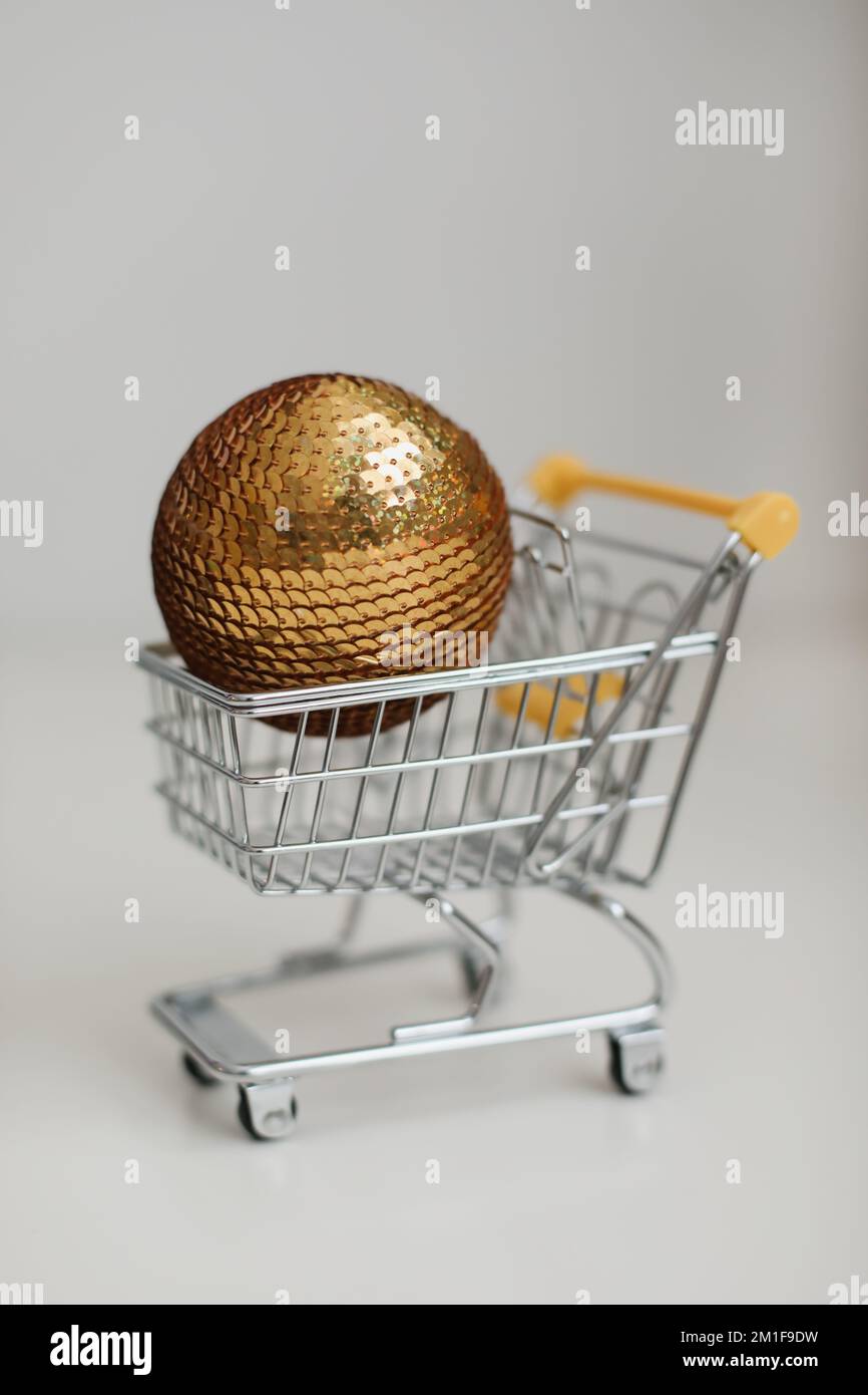 Kleiner Einkaufswagen mit weihnachtsball auf weißem Hintergrund. Kreative Idee für Online-Shopping, Supermarkt, Rabattaktion und Black Friday Stockfoto
