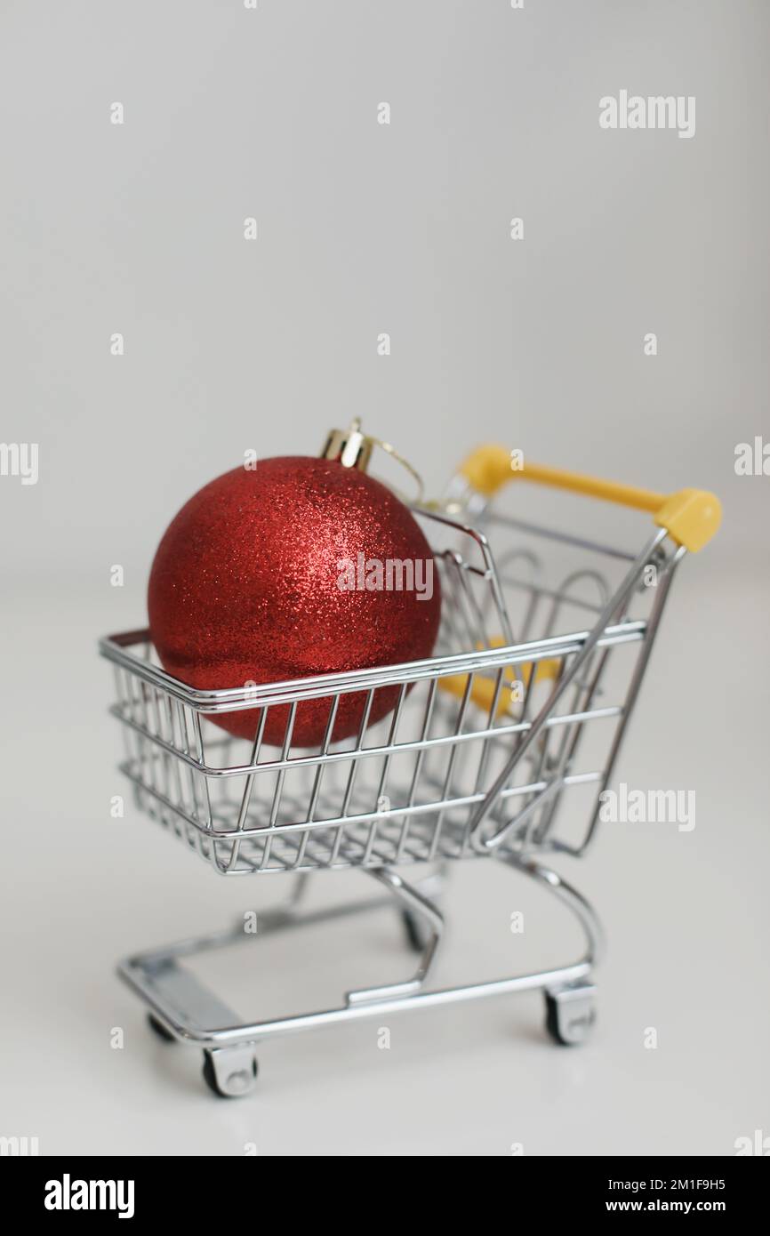 Kleiner Einkaufswagen mit weihnachtsball auf weißem Hintergrund. Kreative Idee für Online-Shopping, Supermarkt, Rabattaktion und Black Friday Stockfoto