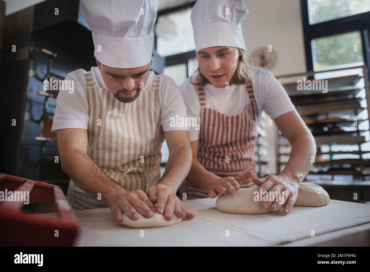 Ein Mann mit daunensyndrom, der mit seinem Kollegen Brot in der Bäckerei vorbereitete. Konzept der Integration von Menschen mit Behinderungen in die Gesellschaft. Stockfoto