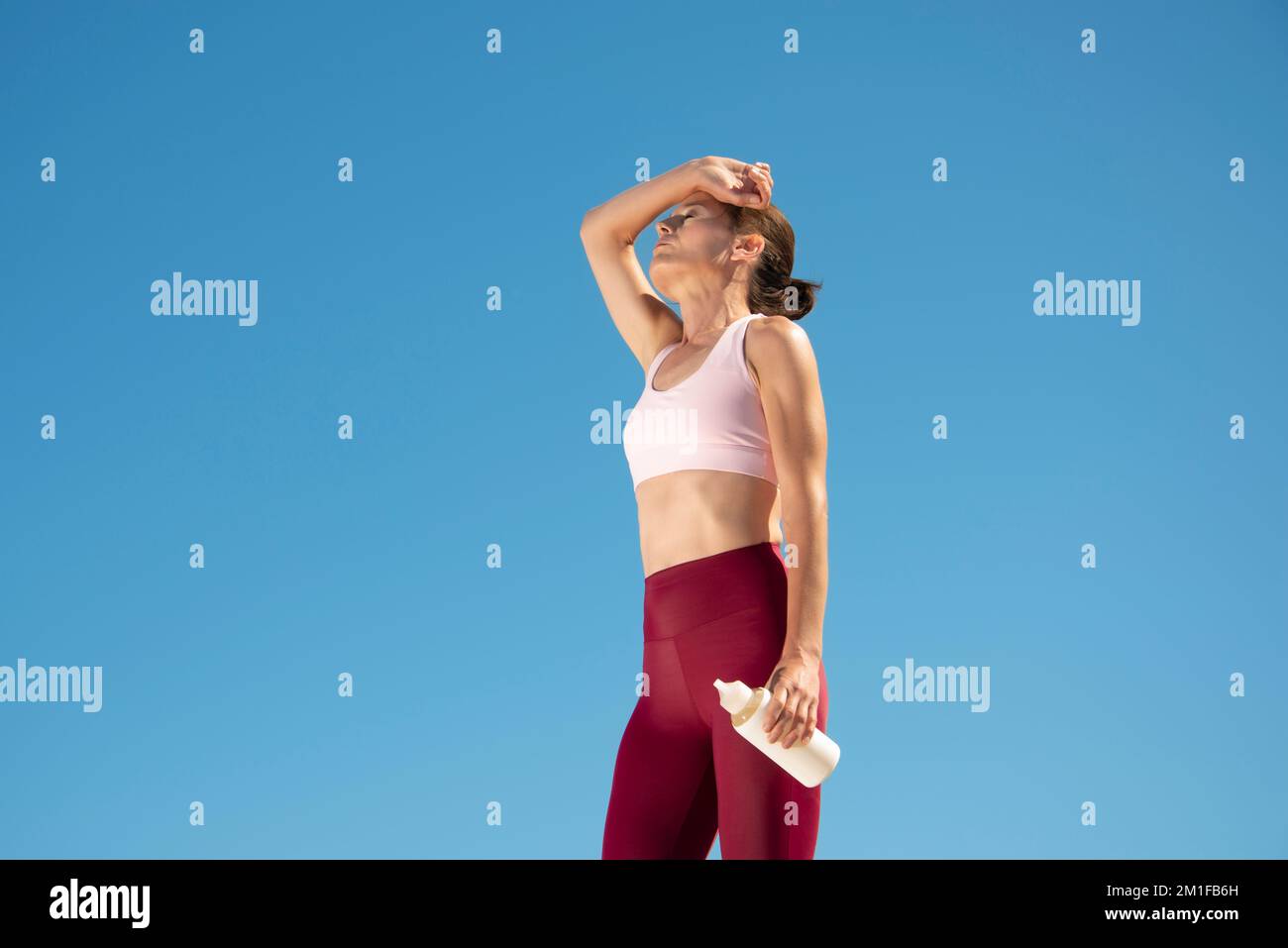 Fit sportliche Frau steht in der Sonne und hält eine Glasflasche Wasser, Hitzewelle Konzept. Stockfoto