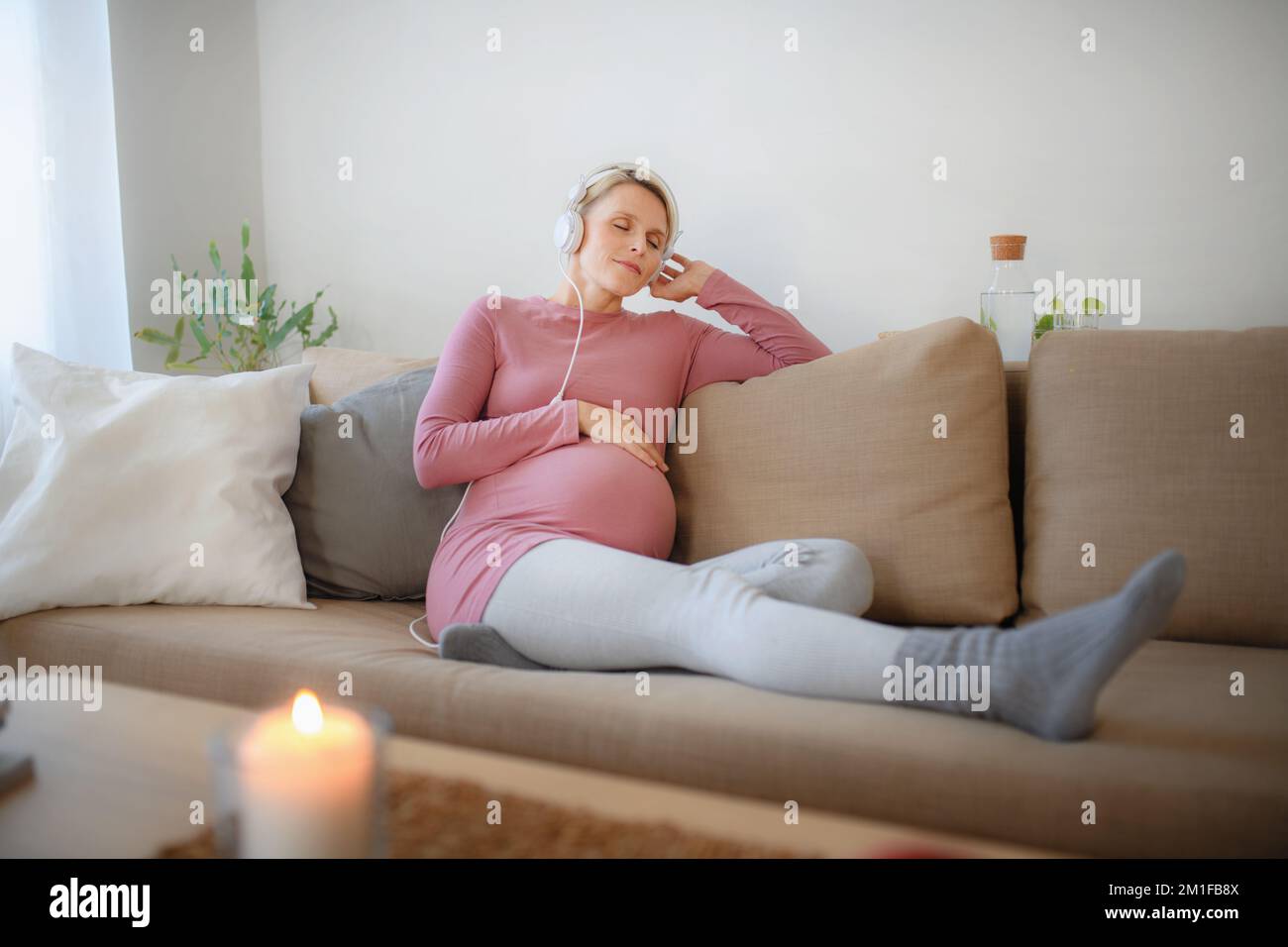 Schwangere Frau sitzt in ihrem Bett, hört Musik und genießt die Zeit für sich selbst. Stockfoto