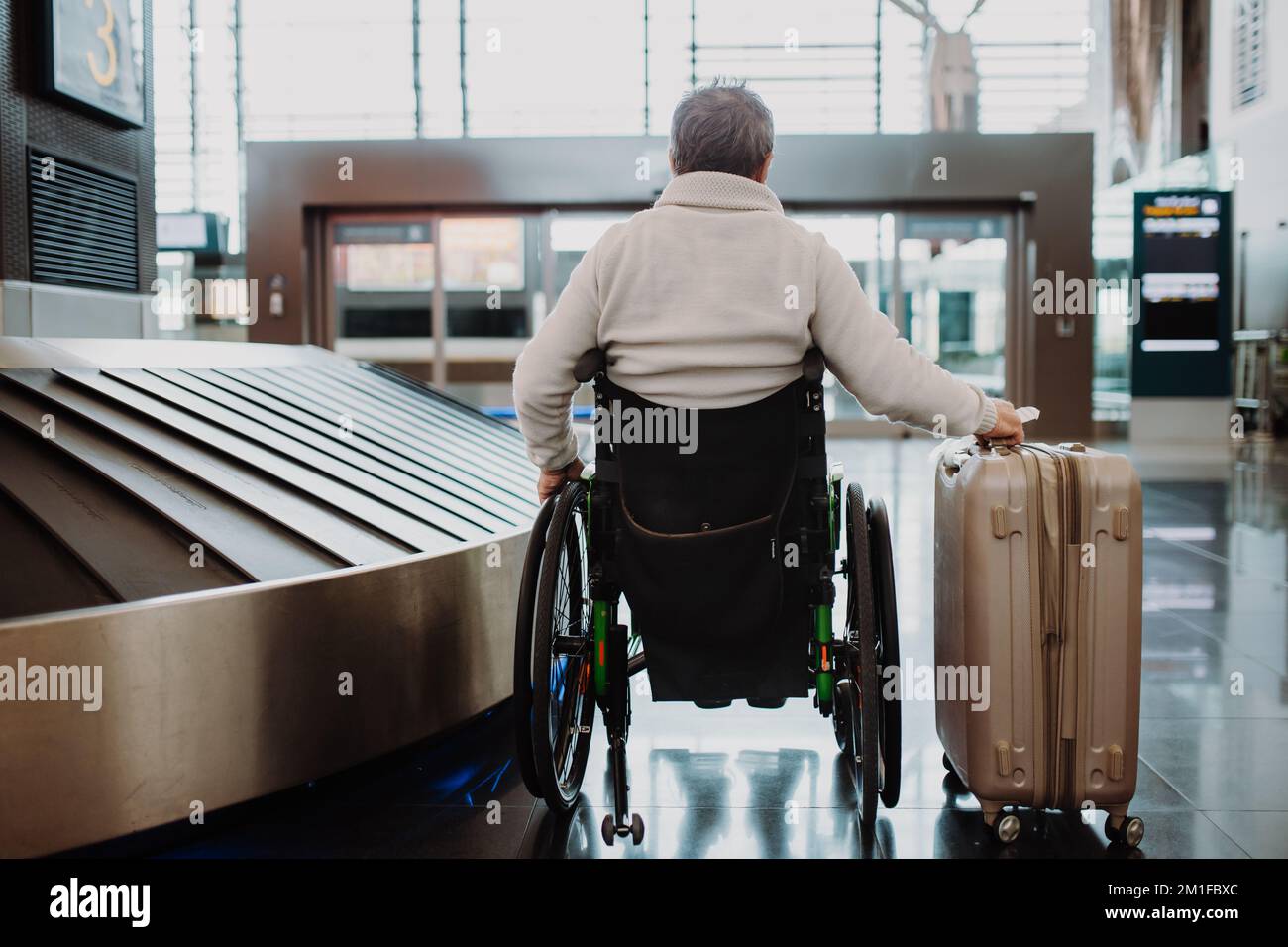 Rückansicht eines Rollstuhlfahrers am Flughafen mit seinem Gepäck. Stockfoto