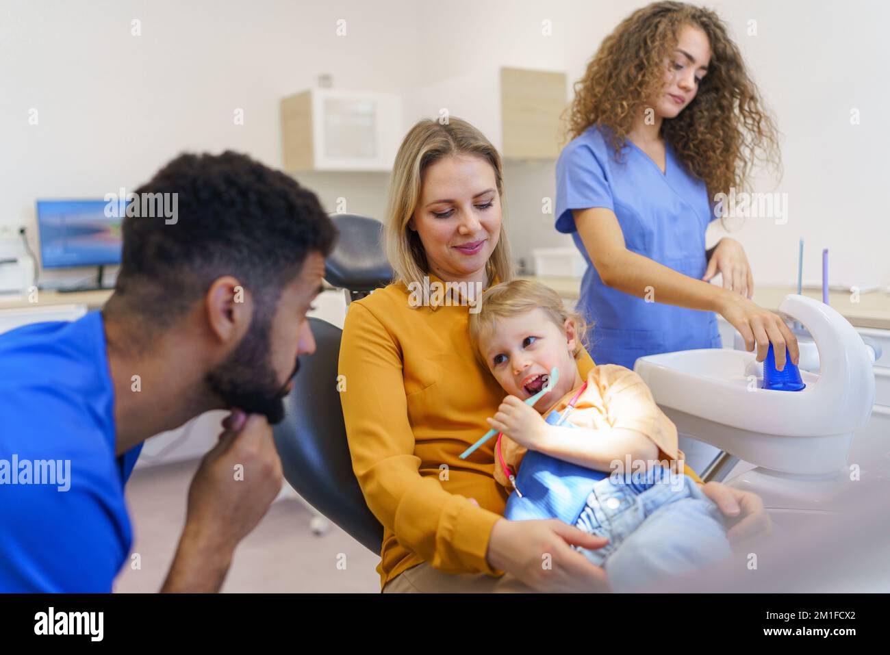 Kleines Mädchen, das mit seiner Mutter auf dem Zahnarztstuhl sitzt, während der Vorsorgeuntersuchung. Stockfoto