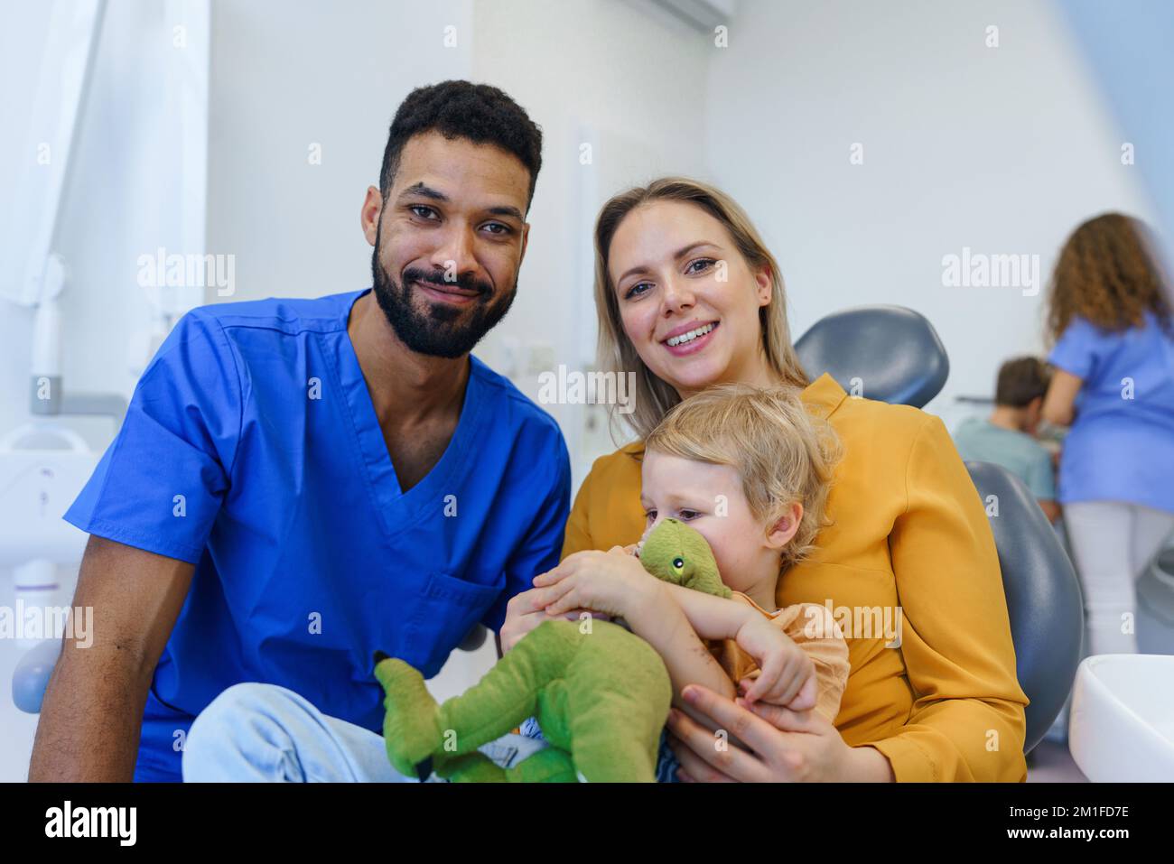 Das Porträt des multirassischen Zahnarztes und der jungen Mutter mit Kleinkind auf dem Zahnarztstuhl. Stockfoto