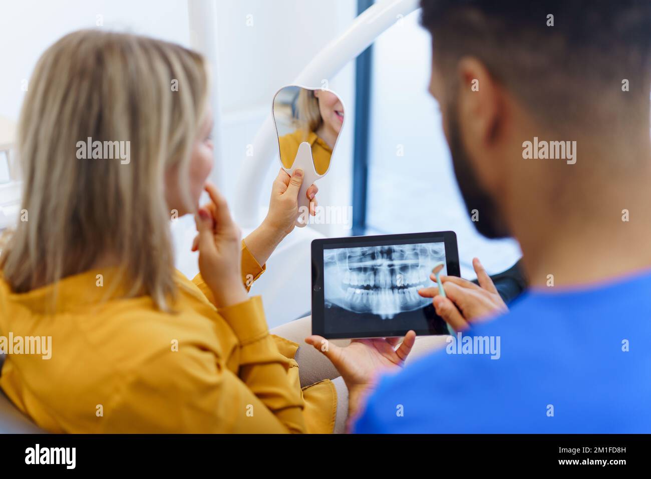 Rückansicht des Zahnarztes mit Röntgenaufnahme am digitalen Tablet für seinen Patienten. Stockfoto
