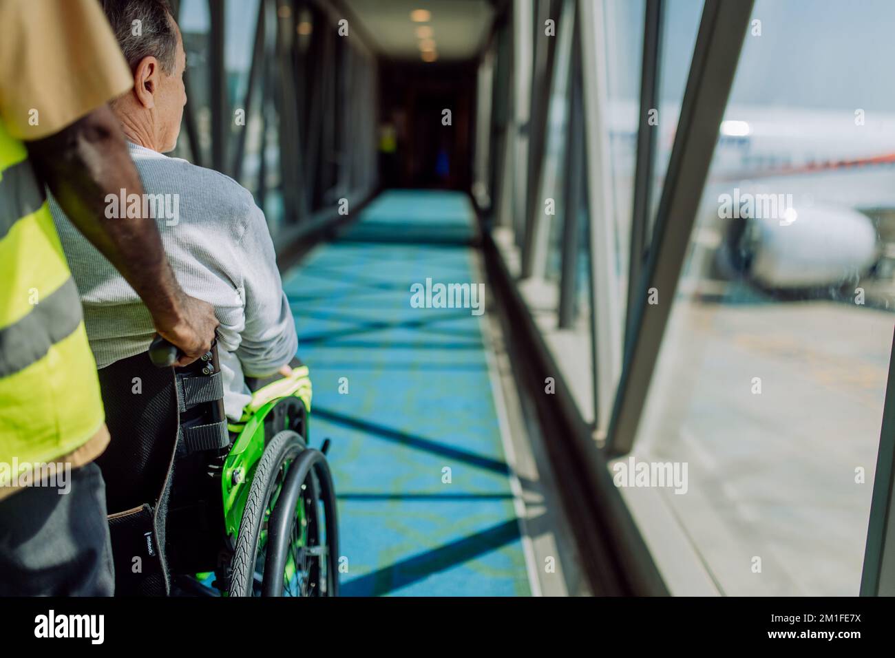 Rückansicht eines Flughafenarbeiters, der einen Rollstuhlfahrer im Flugzeug schiebt. Das Konzept des Reisenden mit besonderen Bedürfnissen. Stockfoto