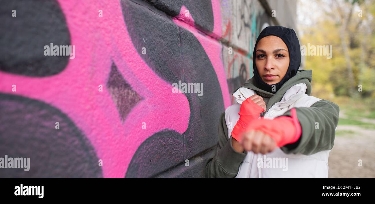 Porträt einer jungen muslimischen Frau mit Sporthandschuhen, die vor Graffiti steht. Stockfoto