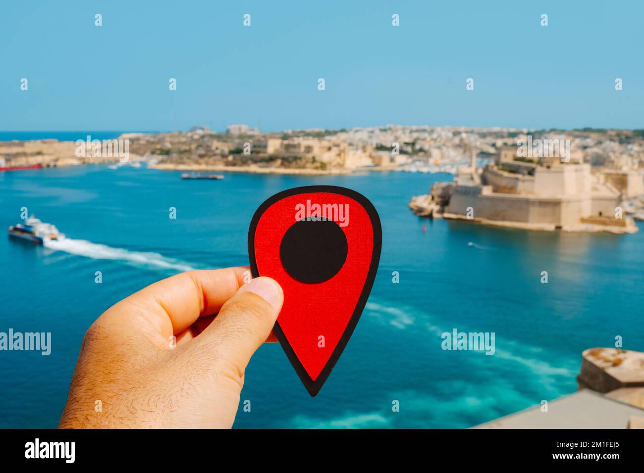 Ein Mann hält einen roten Marker, der auf den Grand Harbour oder Hafen von Valletta in Malta zeigt, mit den drei Städten im Hintergrund, an einem Sommertag Stockfoto