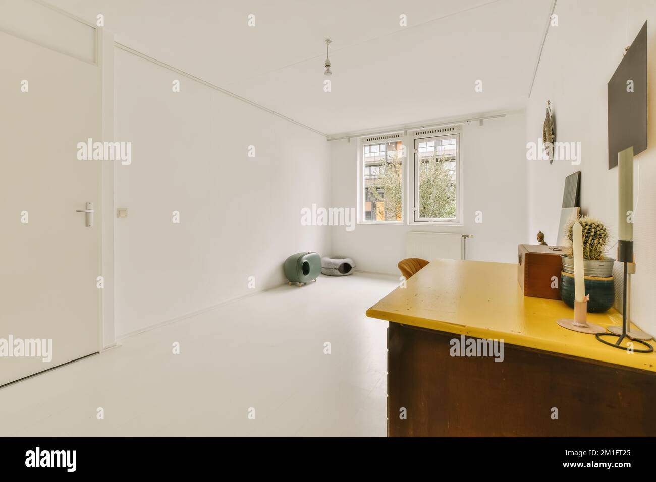 Ein leerer Raum mit weißen Wänden und Holzfußboden, es gibt einen gelben Tisch vor der Tür Stockfoto
