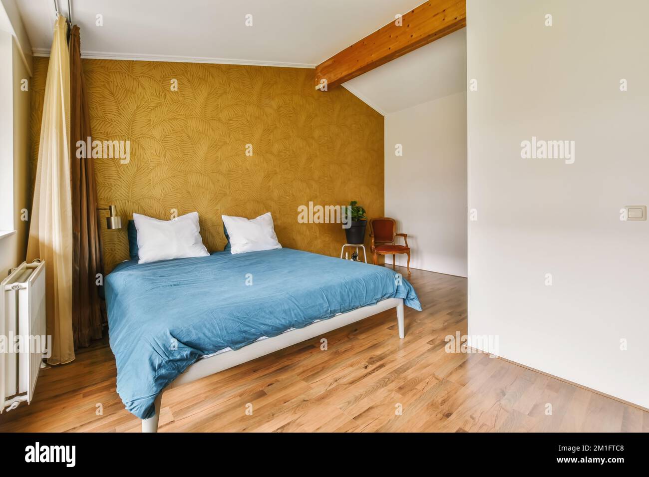 Ein Bett in einem Zimmer mit Holzfußboden und gelber Tapete an den Wänden dahinter ist ein Fenster Stockfoto