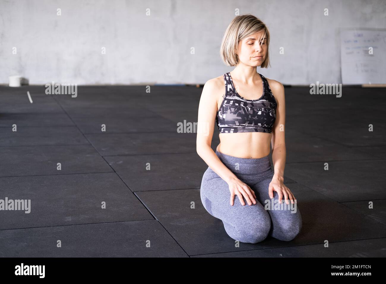 Ganzkörperfoto einer entspannten erwachsenen Frau, die sich im Knien ausruht und meditiert, oder vajrasana-Pose mit geschlossenen Augen während ihres Vinyasa Flow Yoga PR Stockfoto