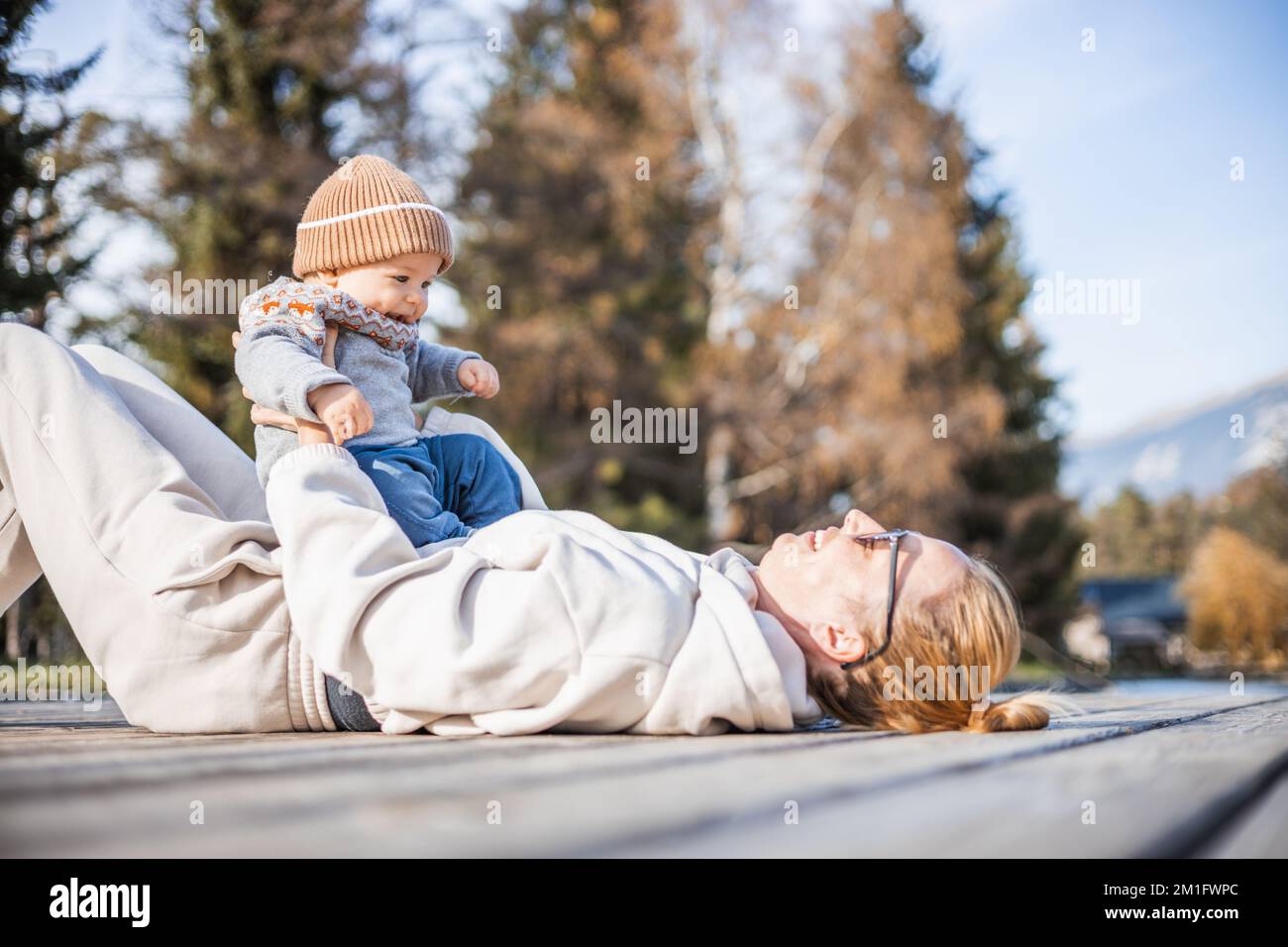 Glückliche Familie. Junge Mutter, die mit ihrem kleinen Jungen an einem sonnigen Herbsttag außerhalb der Tür spielt. Porträt von mutter und Sohn auf einer hölzernen Plattform am See. Positive menschliche Emotionen, Gefühle, Freude Stockfoto